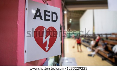 An automated external defibrillator symbol or sign in sport gymnasium.AED using in public emergency situation such as acute cardiac arrest and CPR.Basketball players was playing in blurred background.