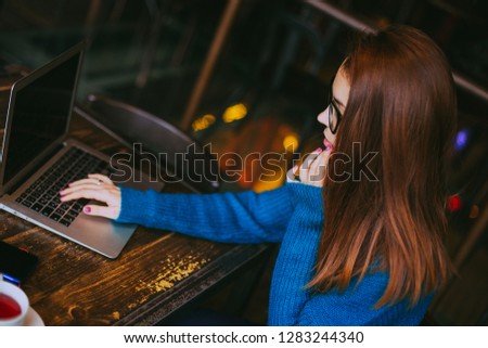 Woman in  the blue sweater uses a laptop at the workplace , working remotely at cafe.