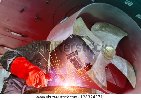 Industry building ship,Welding worker with spark weld factory at shipbuilding and ship, Repairing industrial, wear equipment protective on propeller with rudder of cargo ship background.