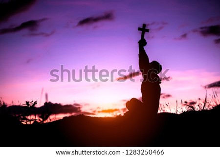 Boy lift the cross up to sky and praying with ligth of sunset 
background, christian silhouette concept.