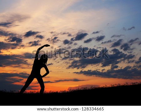 Silhouette of young woman doing exercise over the sunset background