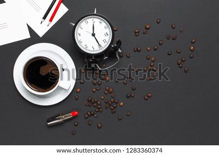 Flat lay cup black coffee, coffee beans, black alarm clock, red lipstick, color pencils, white cards on gray dark background top view copy space. Creative Concept time to work, female desktop