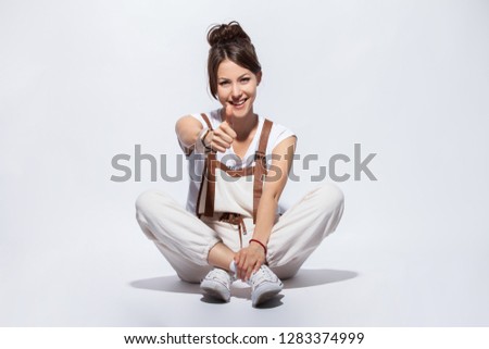 Beautiful young woman sitting on the floor, smiling positive, doing ok sign with hand and fingers. Successful expression.