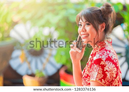 Happy young asian woman wearing Chinese red dress talking on mobile phone with client.