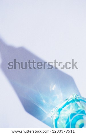 Glass bottle close-up with colorful shadows and flares on a white background. Geometric shapes in photography concept. Direct sunlight flat lay with copy space.