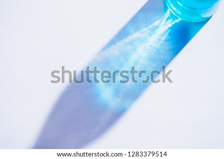 Glass bottle close-up with colorful shadows and flares on a white background. Geometric shapes in photography concept. Direct sunlight flat lay with copy space. Royalty-Free Stock Photo #1283379514