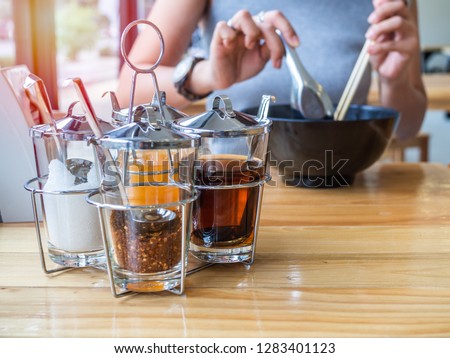 Woman eating a cup of noodles with Thai-style noodles seasoning set, cayenne pepper, sugar, fish sauce, and vinegar on wooden table. Royalty-Free Stock Photo #1283401123