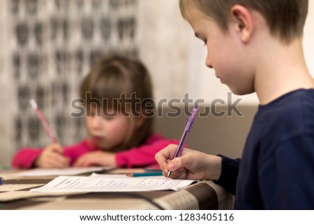 Two cute young children, boy and girl, brother and sister doing homework, writing and drawing at home on blurred background. Art education, creativity and children activities concept.