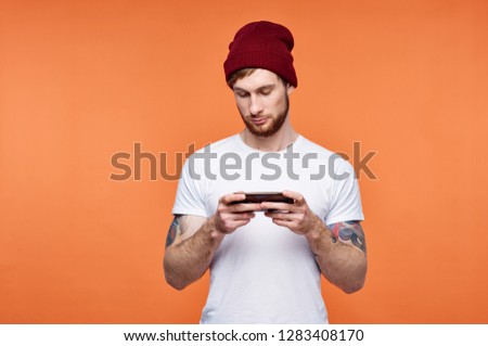 A young man in a knitted hat looks into the phone tattoos on his hands an orange background                 