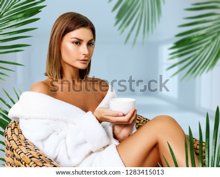 Beautiful woman in bathrobe sitting on the chair and drinking tea in spa salon.