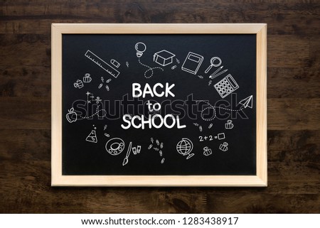 Square framed blackboard with doodles and back to school text over a wooden table background