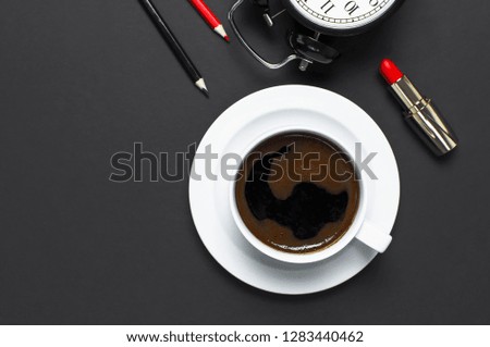 Flat lay cup black coffee, coffee beans, black alarm clock, red lipstick, color pencils on gray dark background top view copy space. Concept time to work, female desktop Minimalistic coffee background