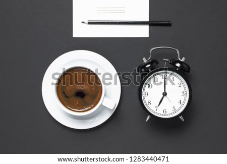 Flat lay cup of black coffee, black alarm clock, pencil, white cards on gray dark background top view copy space. Minimalistic food concept, morning breakfast, time to work hot drink coffee background