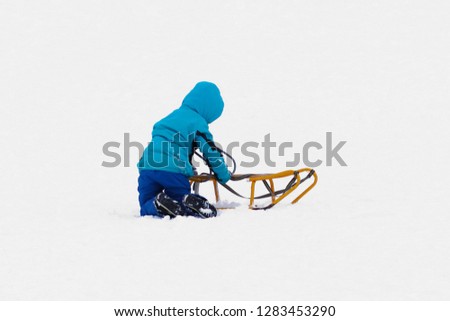 The child rides in the winter on a sled on a snowy street. Activity of the growing up generation in the fresh air. Healthy lifestyle in a cold environment. Hardening children. The joy and fun.