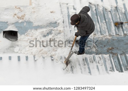 Man clears snow with a wooden shovel, street winter snow removal.