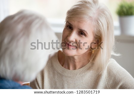 Middle aged female with blonde hair looking at grey haired male, close up focus of woman face. Attentive wife listens her beloved husband sitting together at home spending enjoying free time together Royalty-Free Stock Photo #1283501719