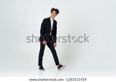 Curly guy in a full-length suit on a light background indoors              