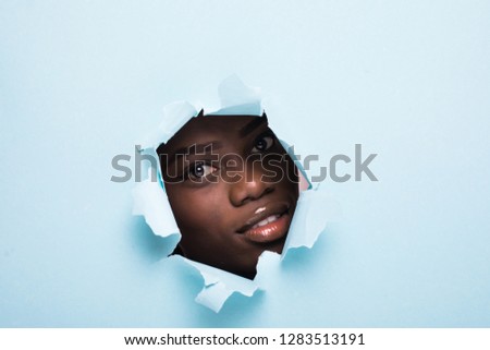 Young afro american woman with make up face skincare inside hole on blue background