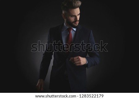 portrait of smart casual man in navy suit looking down to side while standing on black background