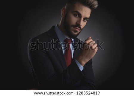 portrait of attractive businessman with beard wearing navy suit while standing on black background