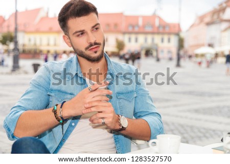 handsome casual man relaxing at table in city looks to side while sitting and fixing rings, portrait picture