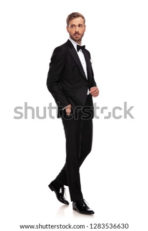 elegant businessman steps to side with hand in pockets on white background and looks to side, full body picture