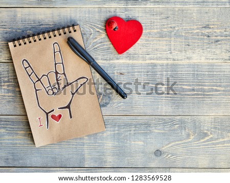 Notebook, which is drawn ASL symbol "I love you" and a wooden red heart with a ladybug. All on textured boards of light blue color. There is a place for designer stickers and inserts.
