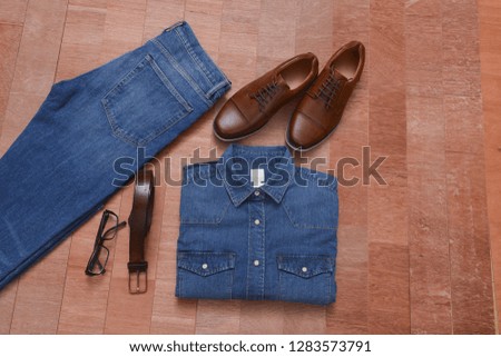 Blue jeans and long sleeve shirts and leather shoes ,belt sunglasses on wooden background