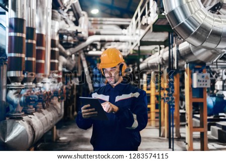Portrait of young Caucasian man dressed in work wear using tablet while standing in heating plant. Royalty-Free Stock Photo #1283574115