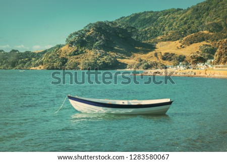Retro-style photo of a wooden row boat moored in calm waters of the bay on a summer day. Green mountain slopes at the distance. Toned image