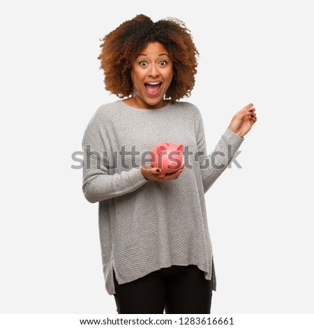 Young black woman holding piggy bank holding something with hand
