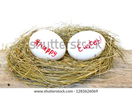 Two chicken eggs in straw nest with text happy Easter and sign hashtag for social network on wooden rough board on white background.