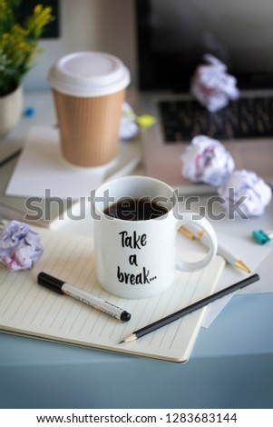 Messy busy working table top shot and coffee mug with printed text " take a break...".