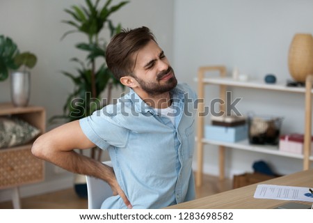 Tired exhausted man feeling pain in back suffering from lower lumbar backache herniated disc after sedentary work, fatigued man rubbing spine muscles sitting in incorrect posture, backpain concept Royalty-Free Stock Photo #1283698582
