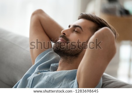 Relaxed happy young man resting having nap on comfortable couch breathing fresh air, lazy tired guy stretching enjoying stress free peaceful day feeling lounge mood at home, peace of mind concept Royalty-Free Stock Photo #1283698645