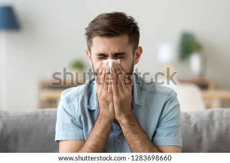 Ill young man sneezing in handkerchief blowing wiping running nose, sick allergic guy caught cold got flu influenza hay fever coughing, having seasonal allergy symptoms respiratory contagious disease Royalty-Free Stock Photo #1283698660