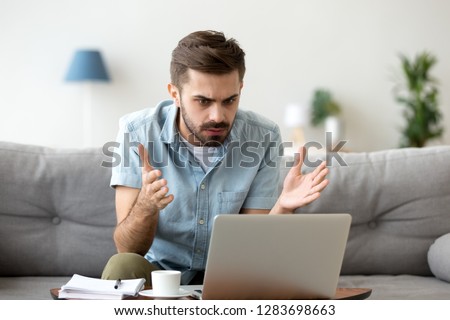 Mad stressed young man angry about stuck laptop or pc failure, furious guy annoyed with computer problem virus, user confused by fake bad online news, frustrated with notebook breakdown or data loss Royalty-Free Stock Photo #1283698663
