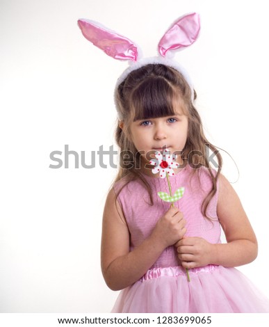 Little girl dressed as the Easter bunny standing on white background and holding flower. Child Easter Holiday Concept. Isolated.