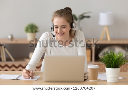 Smiling woman wear headset write notes watch webinar study work on laptop, young student in headphones learning computer course listening lecture training interpreter online teacher translating class Royalty-Free Stock Photo #1283704207