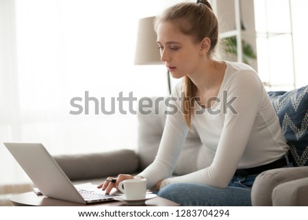 Young woman freelancer using laptop working online making notes, focused teen girl studying on computer writing essay, searching job opportunity, preparing research or coursework in internet at home