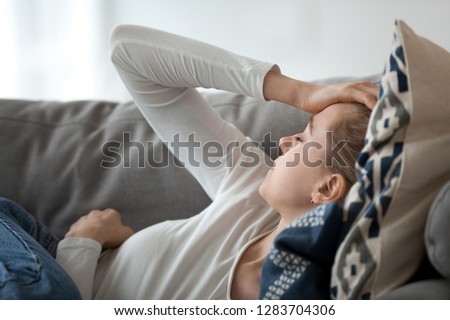 Upset depressed young woman lying on couch feeling strong headache migraine, sad tired drowsy teenager exhausted girl resting trying to sleep after nervous tension and stress, somnolence concept Royalty-Free Stock Photo #1283704306