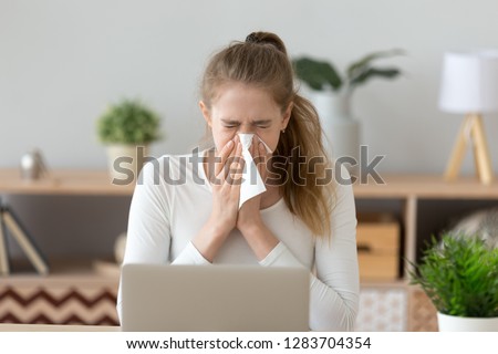 Ill young woman caught cold sneezing in tissue at home or in office, sick allergic girl blowing wiping running nose got flu rhinitis sinusitis coughing, having seasonal allergy symptoms at workplace Royalty-Free Stock Photo #1283704354