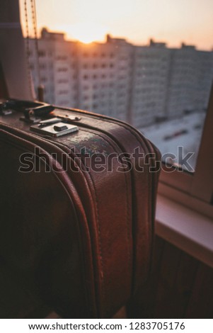Vintage old suitcase standing on the windowsill in front of the window at sunset