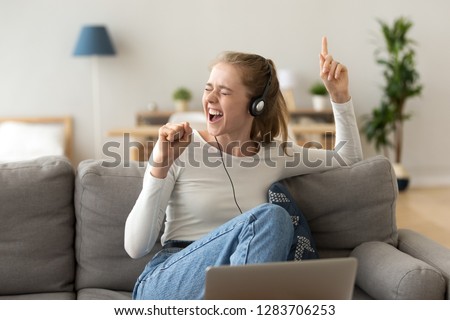 Funky teen girl singing favorite song listening to music podcast in headphones using app at home, happy funny young woman wearing headset enjoying new audio tracks playing in digital application Royalty-Free Stock Photo #1283706253
