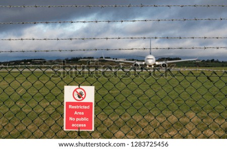 Restricted area sign on fence of airport runway, Passenger aircraft taxiing on runway in the background