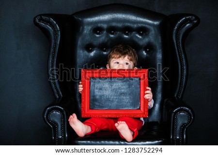 Little boy sitting on the armchair with red framed picture on the St. Valentine's day. little feet close-up.