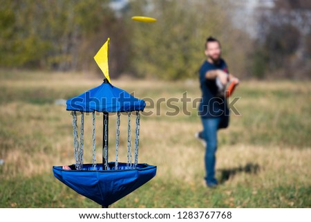 Man throwing flying disk playing disk golf trying to hit disk golf basket