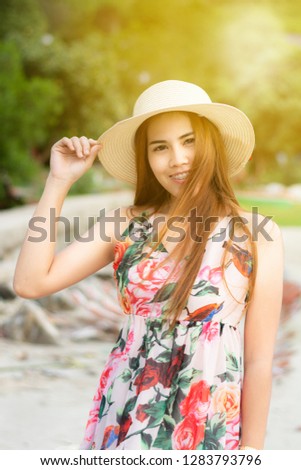 Portrat of asian woman wearing white hat with a flower dress
standing smiling in the outdoors.