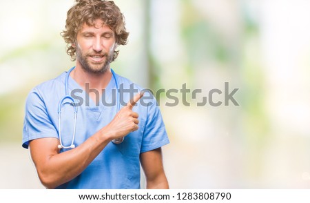 Handsome hispanic surgeon doctor man over isolated background cheerful with a smile of face pointing with hand and finger up to the side with happy and natural expression on face