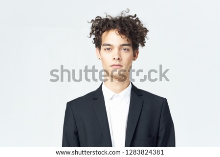 Cute business man in a black suit with curly hair on a light background